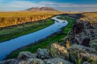 The bright green vegetation lines the Rio Grand River below sandstone bluffs as the San Luis Hills are lit by the rising sun.
