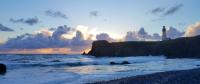 The Yaquina Head headland jutting out into the sea with the Yaquina Lighthouse on top. The sun is setting and the light is a deep blue.