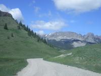 gravel road winding through green hills. rocky mountains in the background. blue skies with a few clouds. 