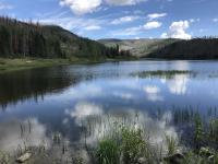 The glassy surface of Shaw Reservoir reflects the sky, clouds, and mountains that surround the lake.