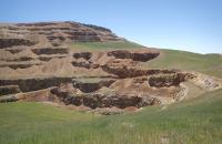 Photo of green grasses growing over the reclaimed Landusky mining operation's August Pit, with the now-grass-covered Gold Bug Butte hillside towering in the background.