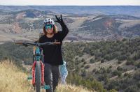 Alan Mandel raises his hand next to his bike with a scenic landscape in the background. 