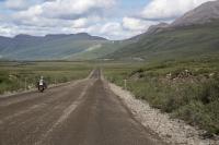 Motorcyclist riding on the Dalton Highway, a strip of gravel road between tundra-carpeted hills. Photo by Bob Wick BLM 2014