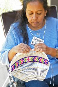 A woman sits and works on a traditional garment with her hands.