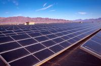 A long row of solar panels in an open area, with a mountain range in the background.