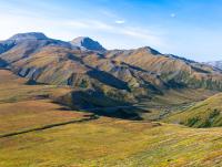 Colorful grassy hills in the foreground with mountains and blue skies. 