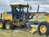 A yellow and black road grader has its windows broken out.