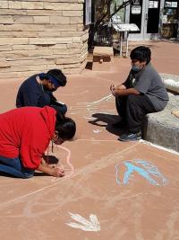 Children create dinosaur chalk art.