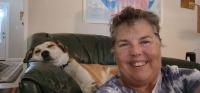 A smiling woman sits in front of a couch where a service dog is resting