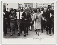 The photo shows Dr. Martin Luther King, Jr. and others walking down a street as part of the Voting Rights March.