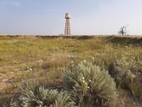 An orange and white color painted water tower sits on the horizon of the lush green Colorado prairie at the site of the former Granada Relocation Center.