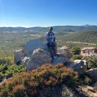 Alexia Williams, who is wearing hiking gear, leans up against a large rock.