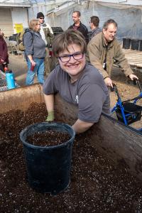 A smiling woman in a gray shirt puts potting soil into a pot. 