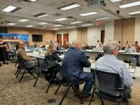 Large meeting room-Members of an advisory council are seated at a long table. 