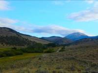 A photo of mountains in the background with a blue party cloudy sky. Grassland is in the foreground. 