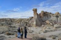 Three people stand on a trail looking at an interesting geological formation called a hoodoo.