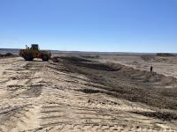 A bulldozer moves dirt. A large area in the foreground is already scraped away.