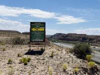 Hanksville Burpee tours sign with desert landscape and road in the foreground. 