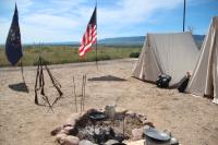 Fire ring in foreground with flags, canvas tents in background. 