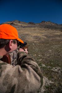 A man aims his rifle at a paper target set up on a hill