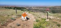 An orange sign that reads Road Closed has been placed in the center of a rugged dirt road with scenic hills and a canyon in the background.