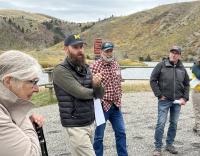 A group of people have a discussion outdoors with hills and a lake in the background