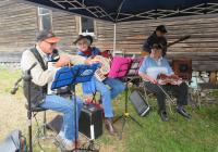 A photo of four people under a pop-up tents with instruments and sheet music. 