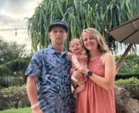 two people, one in a blue shirt and another in a pink dress, holding a baby