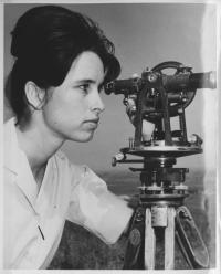 Photo shows a woman looking through a piece of survey equipment. 