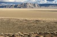 Layers of sagebrush then unvegetated desert playa alternate before a deeply shadowed mountain