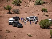 A group of people stand in a circle by vehicles in the red desert.