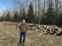 Caucasian man smiles in front of cut stacked logs 
