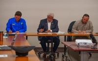 Three men sitting at a long table signing documents. 