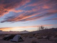 A jeep next to a tent in the desert at sunset. 