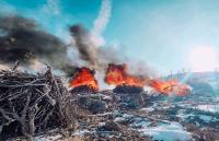 Piles of slash, made up of tree branches and other vegetation, are burning while surrounded by snow on the ground.