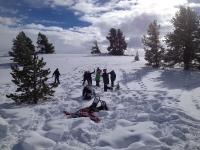 Alt Text: A photo showing several people snowshoeing and playing on a snow-covered hill dotted with juniper trees.