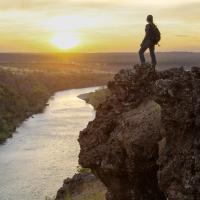 a hiker stands atop a cliff overlooking a river