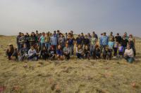 A large group of students and adult pose for a photo in an open, grassy landscape.