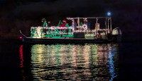 A boat, at night on the water, decorated with lights and people standing on the boat.