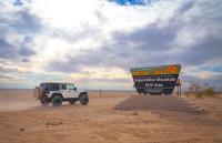 A white jeep drives by a sign reading, 'Superstition Mountains'