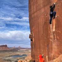 Two climbers on a red sandstone wall in Indian Creek with the clouds in the background.