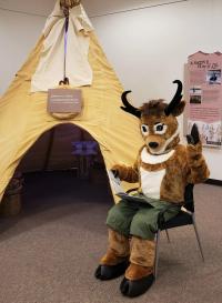 Seymour Antelope sitting with a book outside a tipi. 