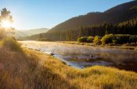 Photo of a river surrounded by grass, trees and mountains at sunrise