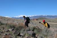 Teenager and adult firefighter hike up a hill with firefighting equipment.
