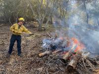 A fire fighter manages a pile of burning brush