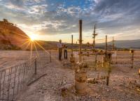 Two BLM employees work near oil and gas pipes with a mountain and the setting sun in the background.