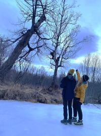 Two women are looking up a hole in the tree while one of them is pointing at it. 