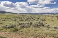 a fence runs through a field of grass and sagebrush leading to distant mountains under a blue, cloudy sky