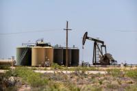Oil pumpjack operating next to large storage tanks in a dry, desert landscape under a clear sky.