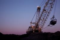 A dragline is silhouetted against a purple and blue sky at an open pit coal mine.